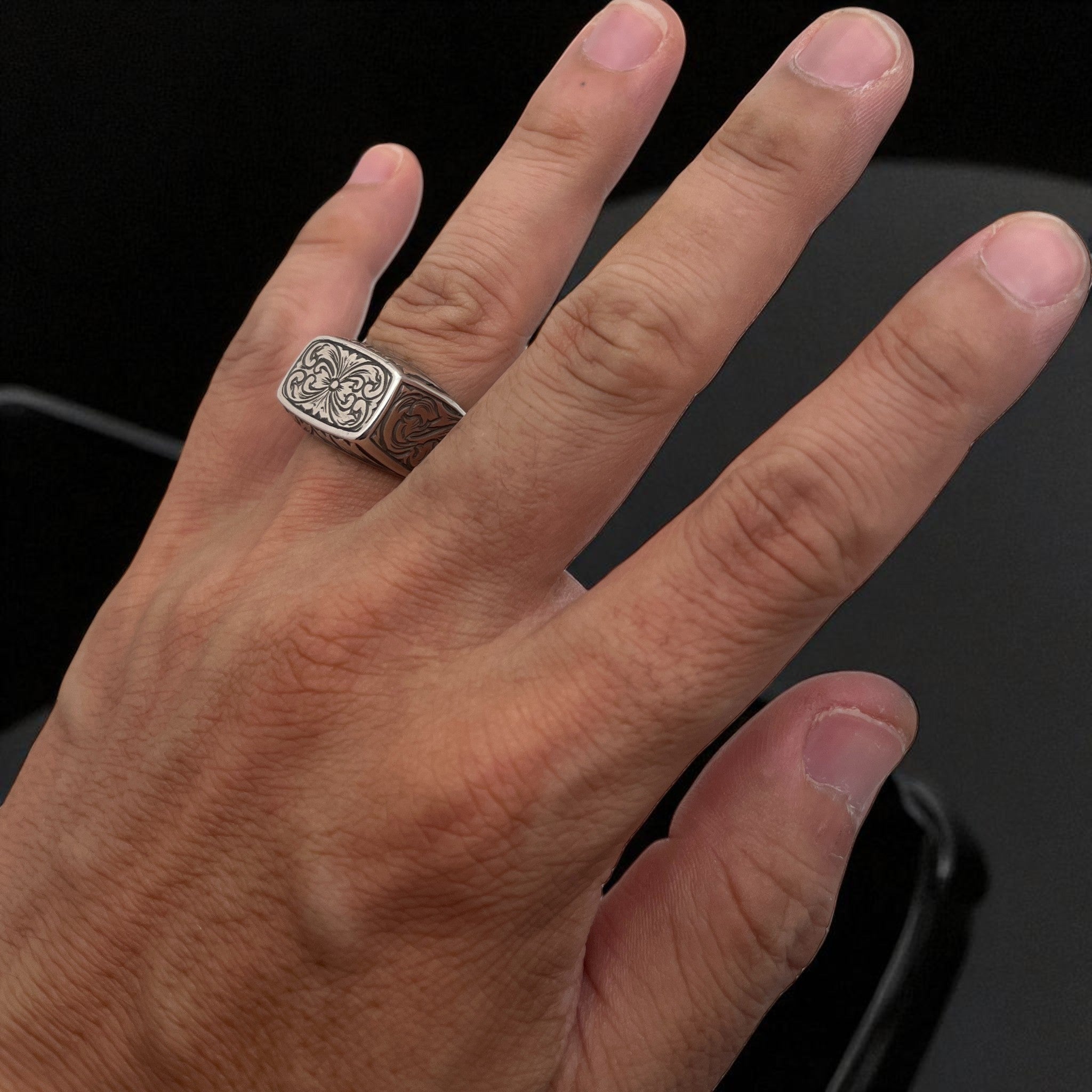 シルバーリング emblem の着用写真。四角いフェイスに彫金されたシンメトリー模様と、側面にまで施されたエングレービングの植物模様を映したデザイン。
