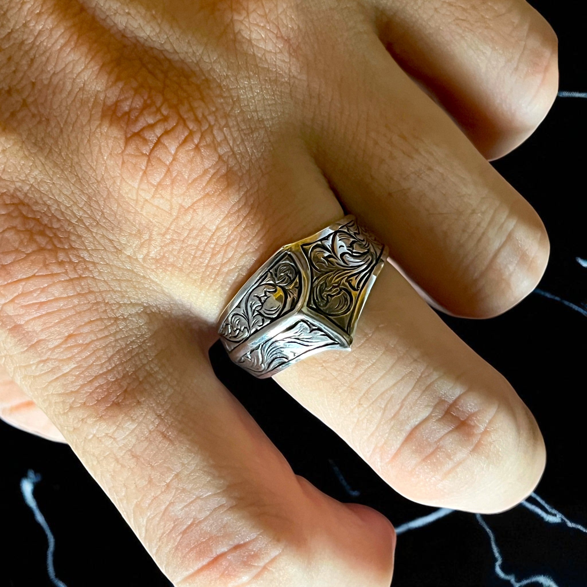 シルバーリング icon の着用写真。シグネットリングの側面から天面にかけて植物模様を細密に彫金したデザインで、立体感と重厚感のある仕上がりを映したイメージ。